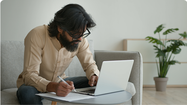 A man looking at a laptop and holding a pen