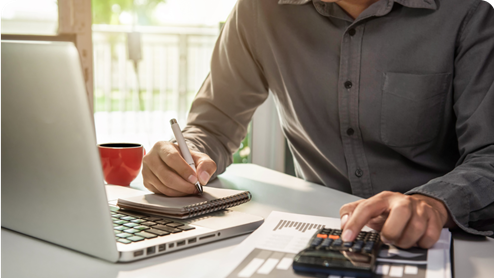 A closeup shot of a man using a calculator and a laptop