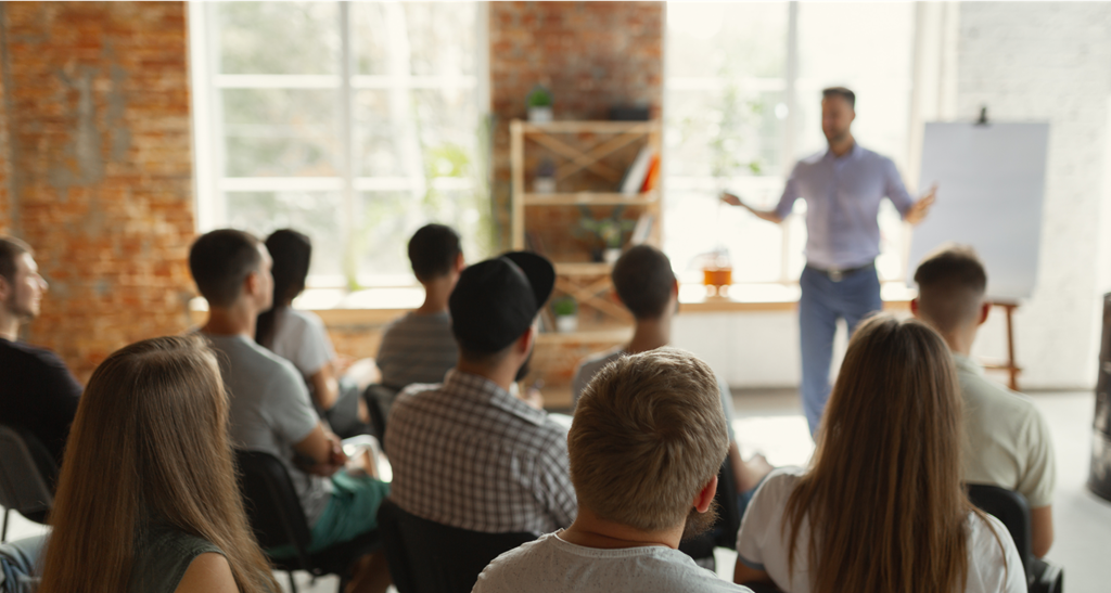 a group of people sitting in front of a speaker in an open office