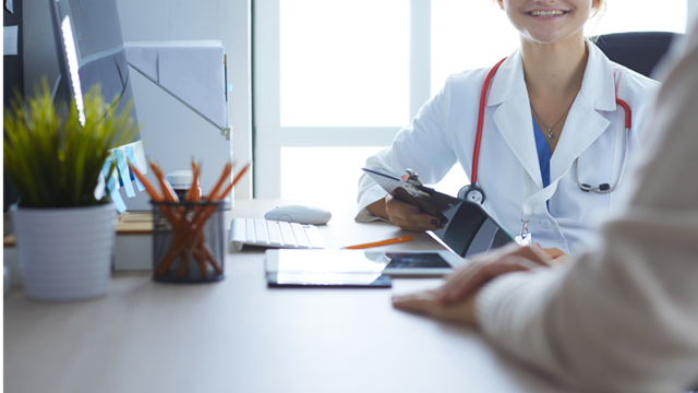  A healthcare worker a in white coat talking with a patient in a hospital setting.