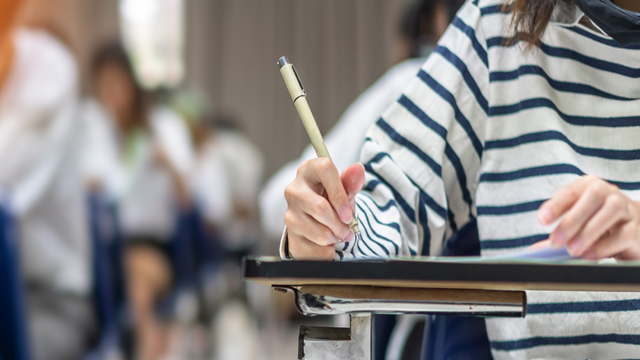 A student writing notes on a paper in a classroom setting.