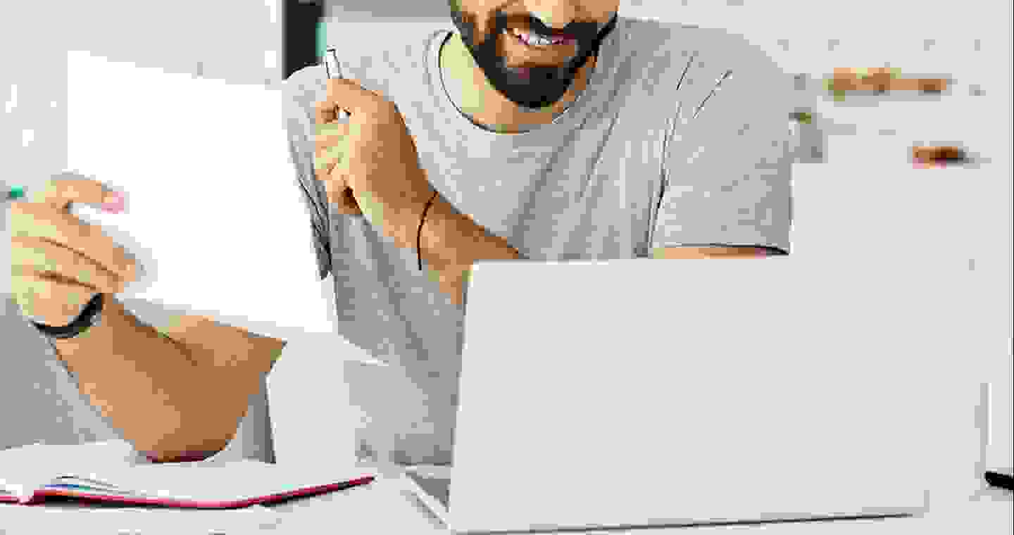 Male looking at laptop paper in hand