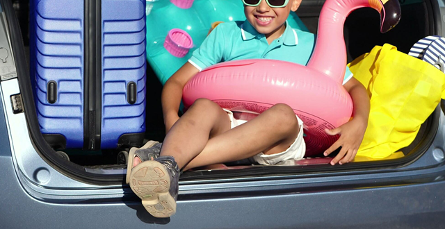 Kid in sunglasses sitting in car boot