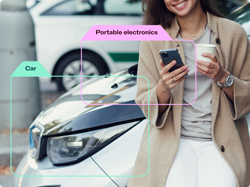 Woman holding a phone and coffee standing in front of a car