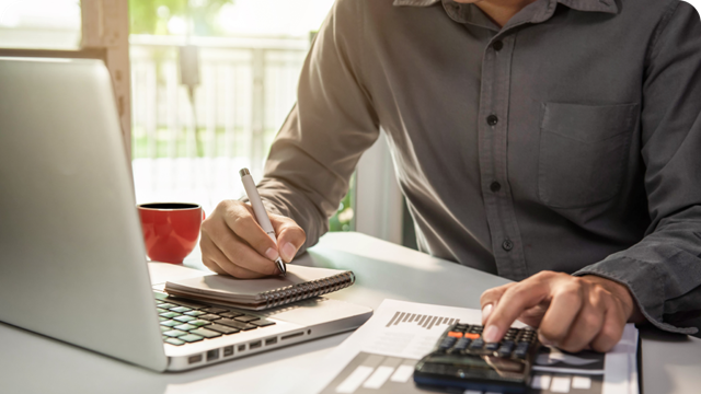 a closeup image of a man using his laptop and calculator